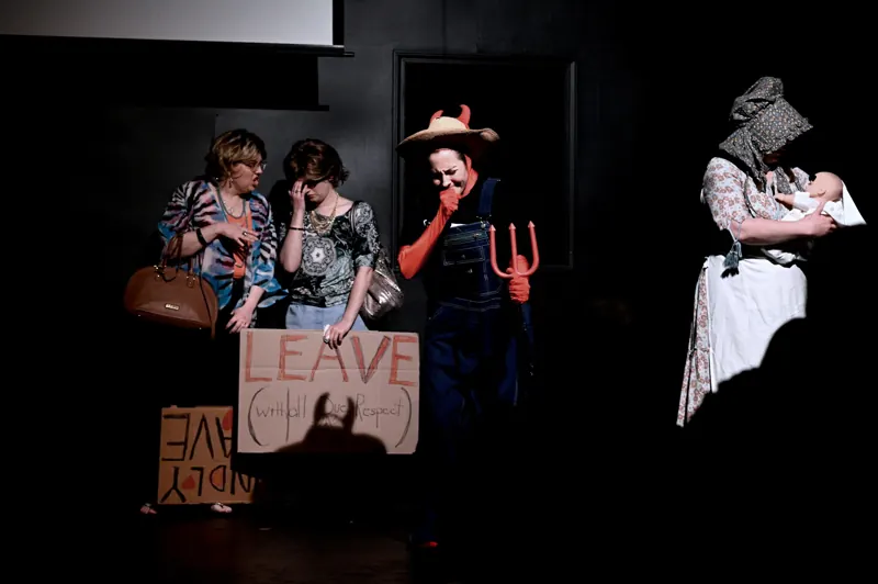Ensemble in costume holding a LEAVE sign, crisp shadows on the back wall