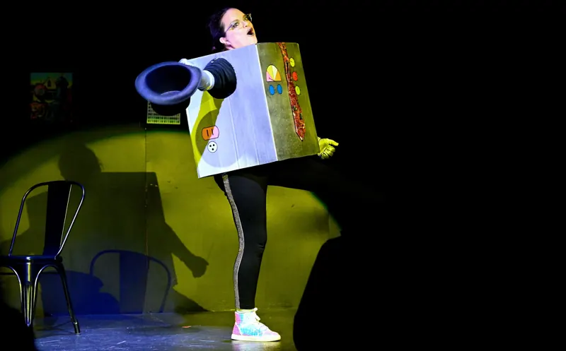 Performer in a costume box under a yellow-green wash with a hard-edged pool of light