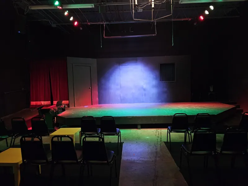 Stage edge glowing green with a soft lavender pool on the back wall and red curtains