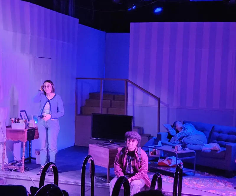 Living-room scene in lavender and magenta, actors spread across the set