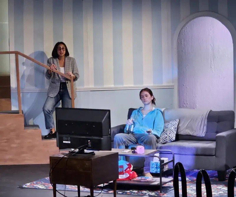 Daytime living-room scene in clean warm-white light, actors on the stairs and sofa